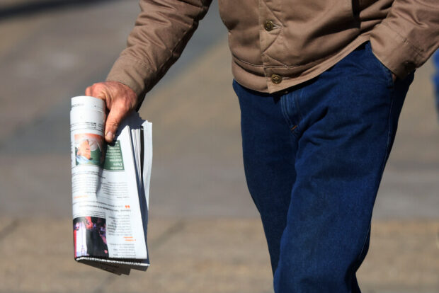 Imagen del torso de un hombre caminando mientras sostiene un periodico.