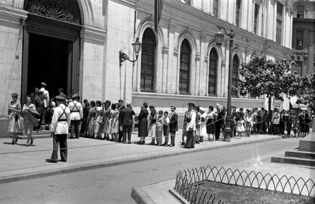 Imagen en blanco y negro de una fila de ciudadanos a las afueras de la Casa Central de la Universidad de Chile para ingresar al funeral de Gabriela Mistral.