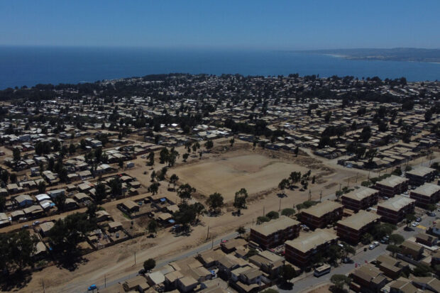 Vista aérea de un asentamiento informal o campamento en una ladera, con el océano y la ciudad al fondo.