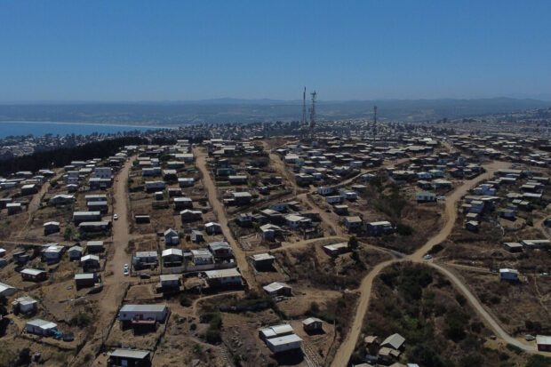 Vista aérea de un asentamiento informal o campamento en una ladera, con el océano y la ciudad al fondo.
