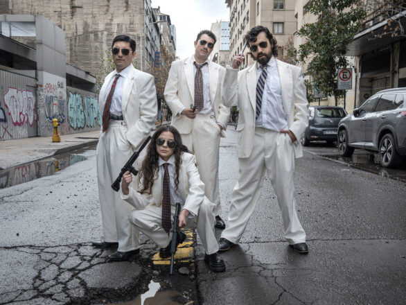 Actores de la obra País Costra vestidos de blanco con armas y lentes oscuros en una calle urbana, durante sesión fotográfica en Santiago.
