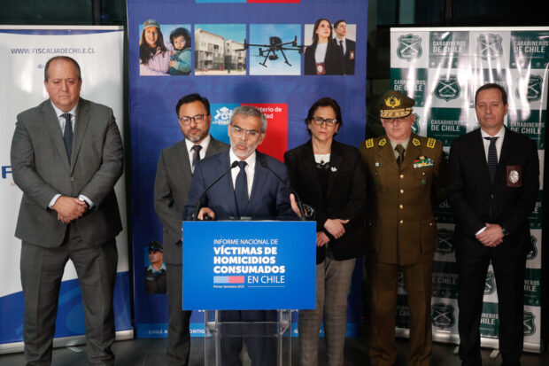 Ministro Cordero habla desde un podio que dice "Informe Nacional de Víctimas de Homicidios Consumados en Chile", detrás de él autoridades de la Fiscalía, Carabineros y PDI.