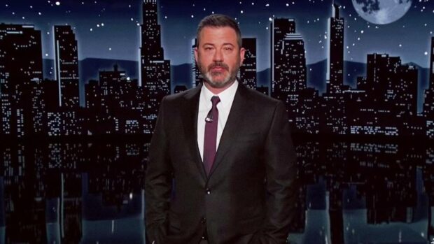 Jimmy Kimmel, presentador de late-night, de pie en el escenario de su programa con el fondo de la ciudad de Los Ángeles por la noche y una luna llena.