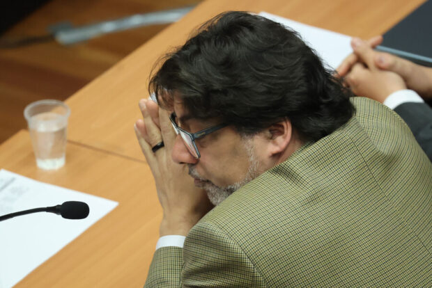 Daniel Jadue sentado en una mesa, inclinado hacia adelante y con las manos unidas a la altura de la boca, con un gesto de atención o concentración durante una audiencia judicial.
