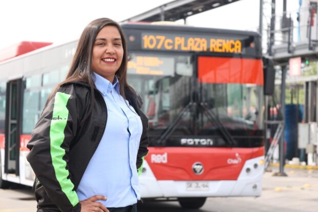 Primer plano de una conductora de autobús, parada frente a un autobús de transporte público moderno rojo y blanco.