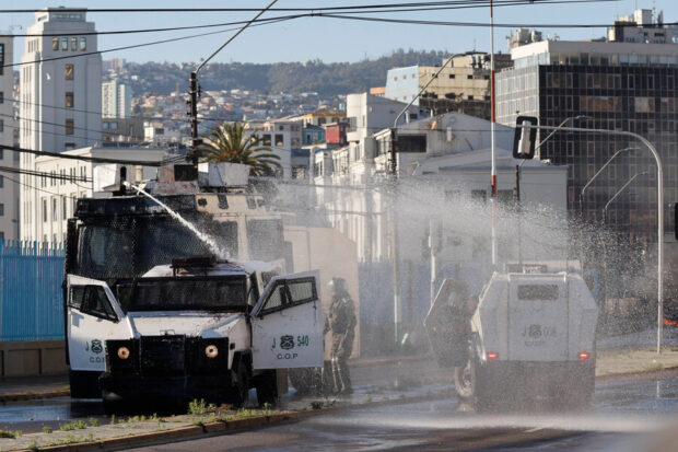 Carros lanza-aguas (zorrillos) de Carabineros de Chile dispersando chorros de agua en una calle de Valparaíso, con edificios de la ciudad en el fondo. Escena de protesta o disturbios.