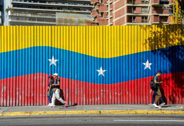 Dos personas caminan delante de una bandera venezolana durante la concentración contra el régimen de Nicolás Maduro antes de su toma de posesión como presidente de Venezuela, a 9 de enero de 2025, en Caracas (Venezuela). 