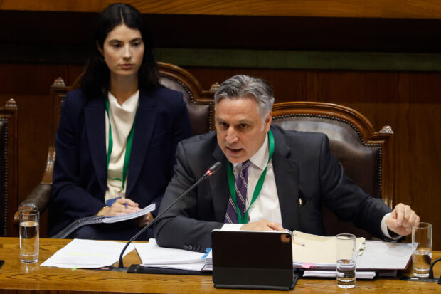 Abogado Francisco Cox habla a través de un micrófono, mientras está sentado en una silla de cuero y tiene una mesa con documentos en la que se apoya.