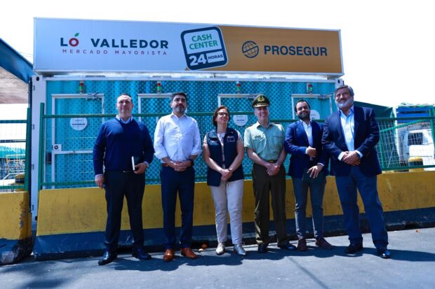 Grupo de cinco personas, incluyendo a la subsecretaria de Prevención del Delito, Carolina Leitao (con chaleco azul marino), el gerente general de Lo Valledor, Marcelo de Moras (camisa blanca), y un oficial de Carabineros de Chile, caminando juntos en el área exterior del Mercado Mayorista Lo Valledor. Al fondo, se ven estructuras metálicas y un letrero que dice "BODEGA SAN RAMON".