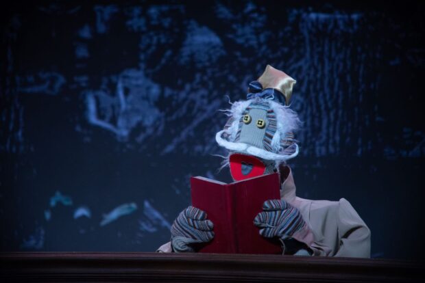 Personaje de 31 Minutos sobre el escenario, leyendo un libro rojo durante el espectáculo Don Quixote en Teatro del Lago, con iluminación teatral y atmósfera nocturna.