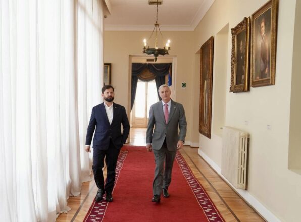 Gabriel Boric y José A Kast caminando por un pasillo con alfombra roja y cuadros en una de la paredes en La Moneda