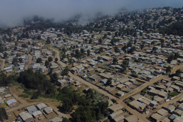 Vista aérea de un asentamiento informal o campamento en una ladera, con el océano y la ciudad al fondo.