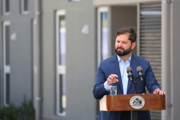 Presidente Gabriel Boric habla desde un podio de madera. Detrás de él se ven las paredes grises de viviendas sociales