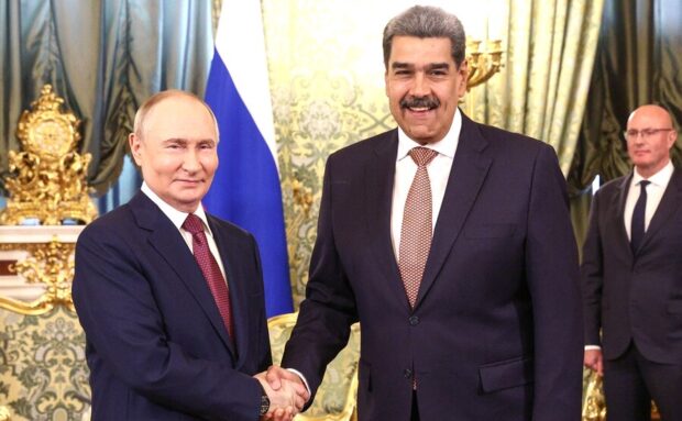 Vladimir Putin y Nicolás Maduro sonrien y se estrechan de manos mientras posan para una foto.