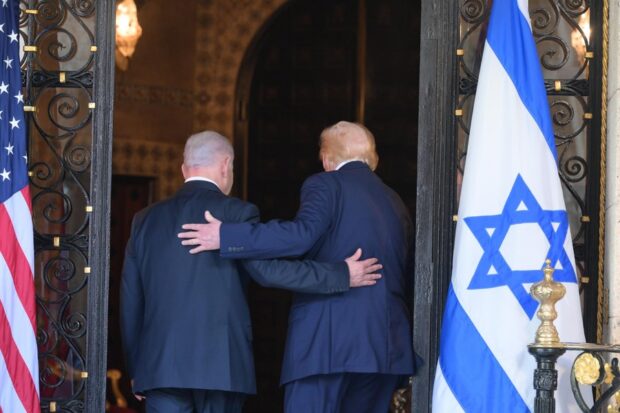 Primer ministro de Israel, Benjamín Netanyahu, y el presidente de Estados Unidos, Donald Trump, de espaldas abrazados. A sus costados se ven las banderas de Israel y Estados Unidos.