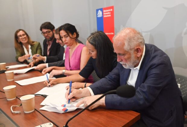 Tres mujeres y dos hombres sentados en una mesa mientras firman papeles.