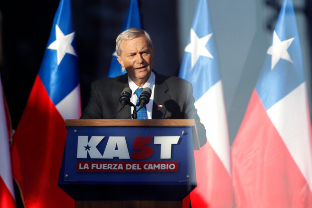 josé antonio kast habla desde un podio que dice: "KAST LA FUERZA DEL CAMBIO". Detrás de él se ven varias banderas de Chile.