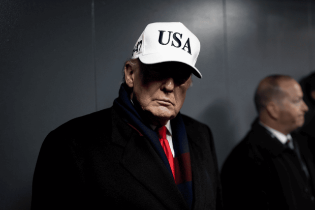 Presidente de Estados Unidos, Donald Trump, usando un jockey blanco con las siglas USA. El gorro hace que sea vea una sombra en la mitad de su rostro.