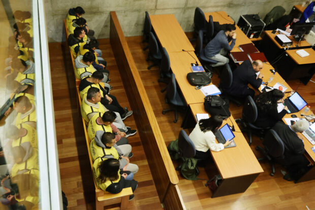 otografía tomada desde arriba de unas 10 personas sentadas en tres banquillos de un jurado, todos vestidos con chaleco amarillo.