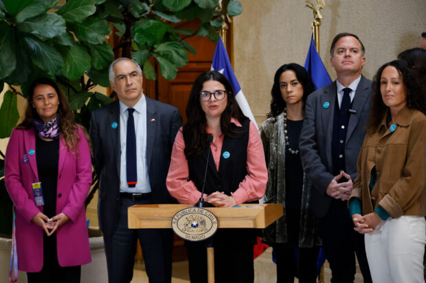 Ministra Orellana habla desde un podio, detrás de ella parlamentarios de derecha y dirigentas sociales.