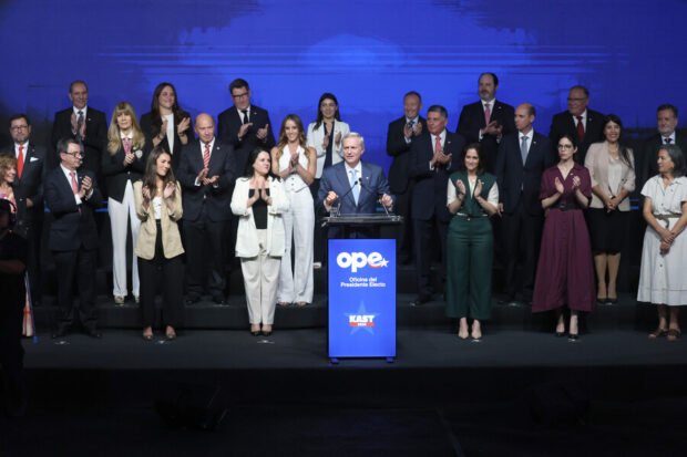 Kast habla desde un podio con un grupo de personas ordenadas atrás de él.