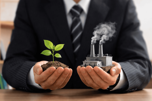 Empresario con traje sostiene en sus manos una planta verde y una fábrica humeante, simbolizando la dualidad entre protección del medio ambiente y explotación industrial en la toma de decisiones empresariales.