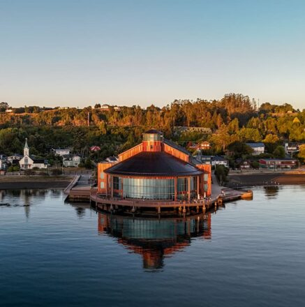 Vista panorámica del Teatro del Lago, una edificación de madera y vidrio inserta en mitad de un lago y rodeado por vegetación.