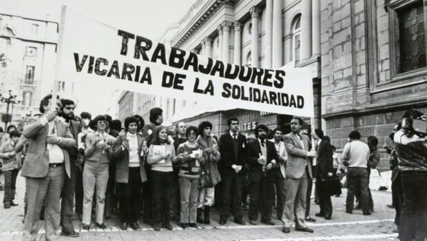 Imagen en blanco y negro de Trabajadores de la Vicaría de la Solidaridad sosteniendo un lienzo que dice "Trabajadores Vicaría de la Solidaridad".