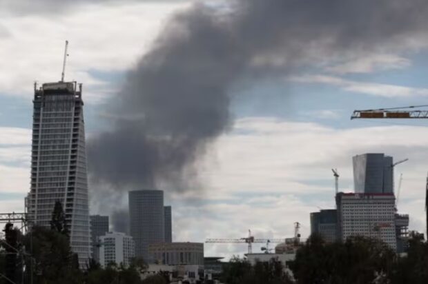 Un rascacielos y otros edificios de una ciudad desde donde se desprende una cortina de humo negra.