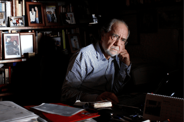 Manuel Antonio Garretón en un escritorio, detrás un biblioteca llena de libros.