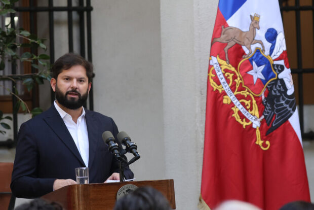 Presidente Boric habla desde un podio de madera, al lado la bandera de Chile con el escudo nacional.