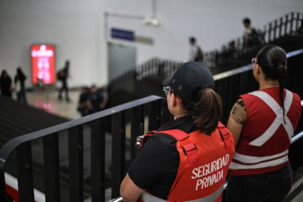 Guardias de metro bajandas unas escaleras y usando chalecos rojos que dicen SEGURIDAD detrás.