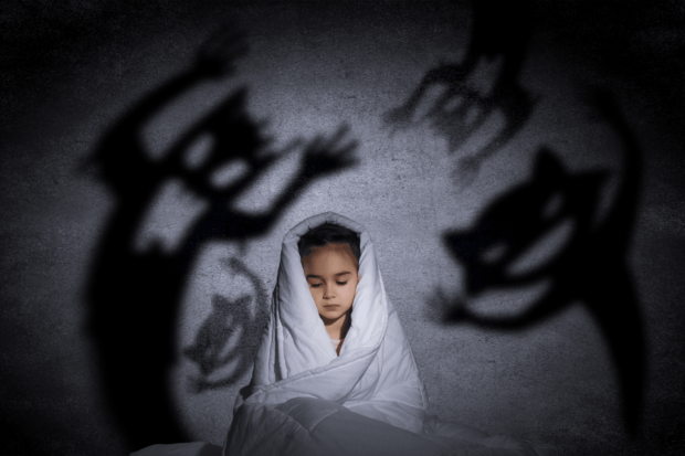 Imagen de una niña cubierta con una sábana y asustada por siluetas fantasmas.