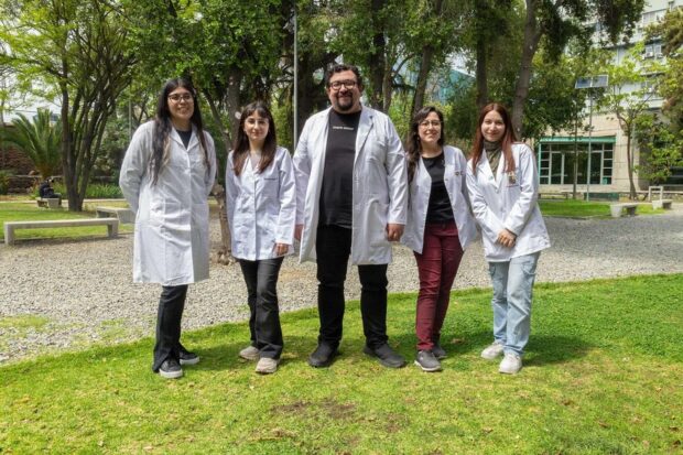 Cuatro científicas y un científico con batas blancas posan para una foto en un patio con pasto.