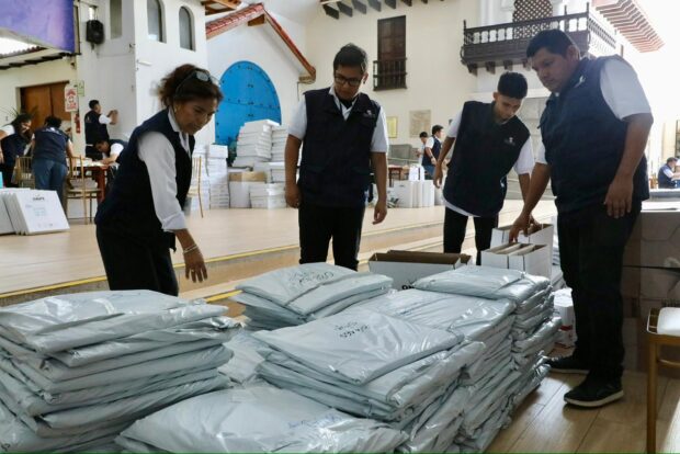 Personal de la ONPE, vestidos con chalecos institucionales azules, organizan paquetes de actas electorales sellados en bolsas plásticas grises.