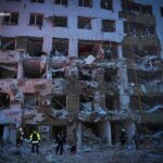 Fachada de un edificio residencial severamente dañado por un ataque, con ventanas destruidas, muros colapsados y marcas de impactos balísticos.