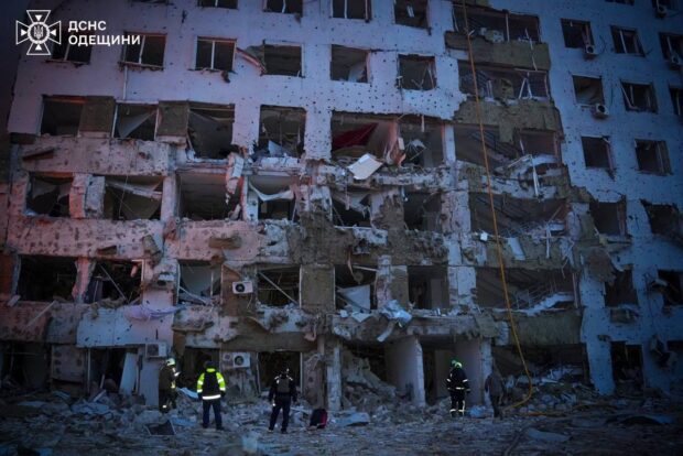Fachada de un edificio residencial severamente dañado por un ataque, con ventanas destruidas, muros colapsados y marcas de impactos balísticos.