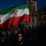 Una mujer con lentes oscuros sujeta una bandera de Irán.