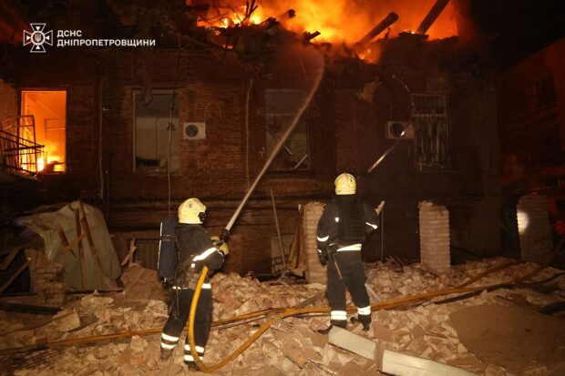Bomberos ucranianos trabajan entre escombros frente a un edificio de ladrillos en llamas.
