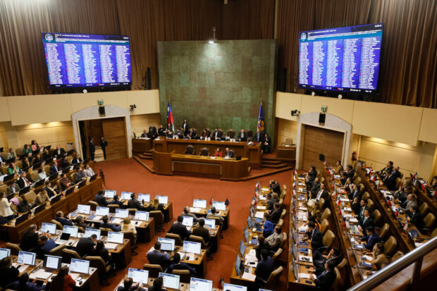 Vista general de una sesión en la sala de la Cámara de Diputadas y Diputados de Chile en Valparaíso, con parlamentarios en sus escaños y pantallas laterales mostrando resultados de votación.