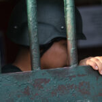 Imagen detalle de un gendarme con casco detrás de una reja.