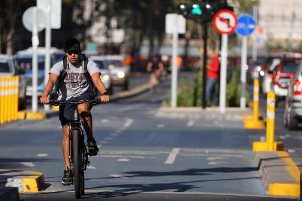 Hombre pedaleando en la ciclovía Nueva Alameda Providencia. Se ve el ciclista al medio mientras los autos siguen su curso a cada lado de la ciclovía.