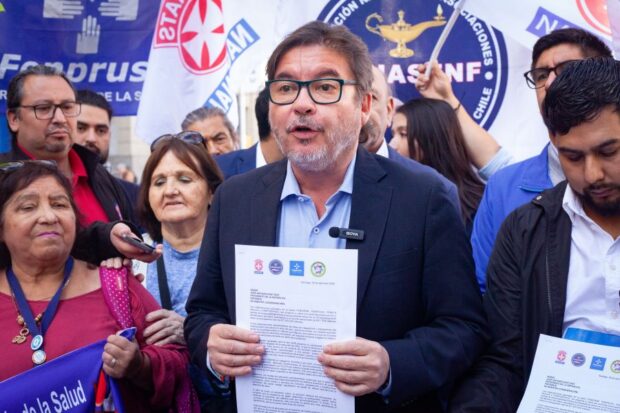 El diputado Marcos Barraza sostiene una carta con las dos manos y está rodeado por representantes de los gremios de la salud.