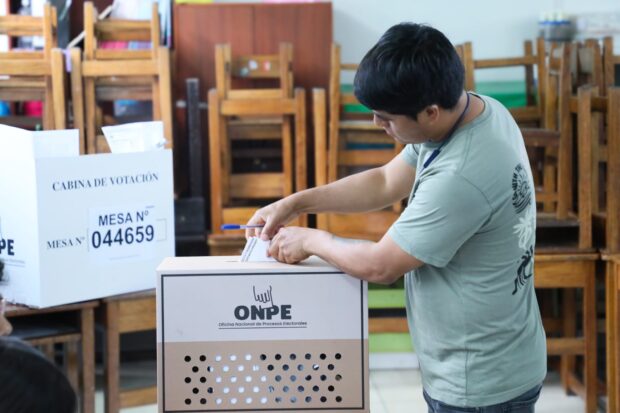 Hombre deposita su voto en una urna de cartón con el logo "ONPE Oficina Nacional de Procesos Electorales".