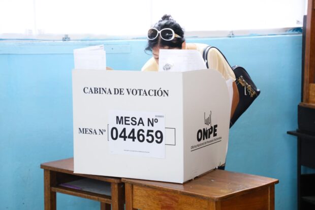 Una mujer emite su voto detrás de un separador de cartón que dice "Cabina de votación".