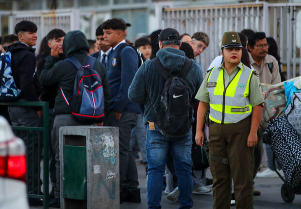 Un grupo de estudiantes al costado una carabinera controlando el paso de vehículos.