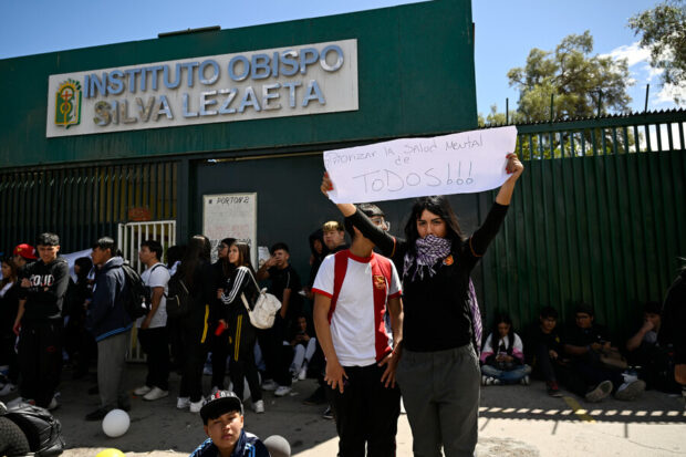 Estudiantes reunidos frente al frontis de un colegio. Una sostiene una pancarta que dice "Priorizar la salud mental para todos".