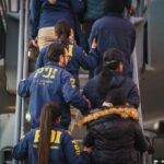 Oficiales PDI custodian fila de personas expulsadas del país mientras suben un avión de la Fuerza Aérea de Chile.