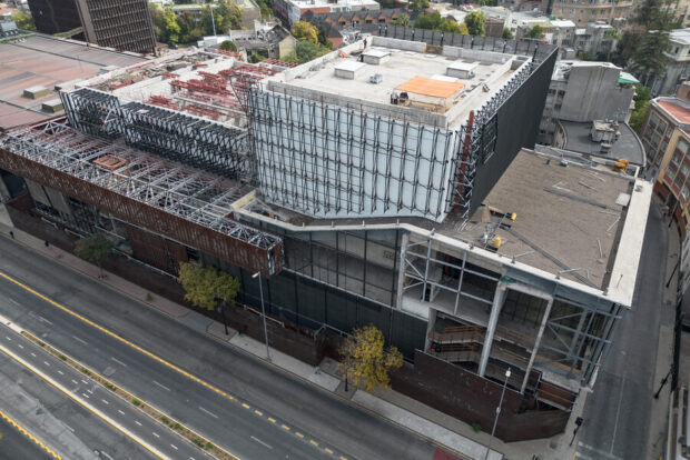Vista aérea de las obras de ampliación del Centro Cultural Gabriela Mistral (GAM) en Santiago. Se observa la estructura metálica y de hormigón rodeada de andamios frente a la Alameda, con la Torre Telefónica de fondo.