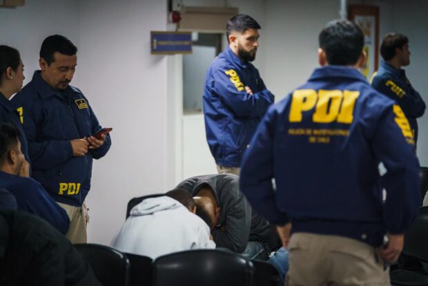 Oficiales PDI custodian a personas expulsadas del país mientras en un cuarto con paredes blancas.
